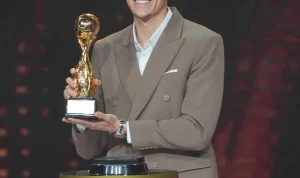 Jay Idzes mengenakan setelan jas berwarna cokelat muda sedang memegang trofi emas PSSI Awards 2026 dengan senyum bangga di atas panggung Jay Idzes mengenakan setelan jas berwarna cokelat muda sedang memegang trofi emas PSSI Awards 2026 dengan senyum bangga di atas panggung.