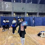alya-rubiya-yuki-medali-perak-kejurnas-anggar-2026 Atlet anggar putri Alya Rubiya Yuki mengenakan hijab hitam dan jaket olahraga, berdiri di tengah lapangan GOR sambil memegang sertifikat Juara 2 dan menunjukkan medali peraknya.