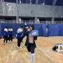 Atlet anggar putri Alya Rubiya Yuki mengenakan hijab hitam dan jaket olahraga, berdiri di tengah lapangan GOR sambil memegang sertifikat Juara 2 dan menunjukkan medali peraknya.