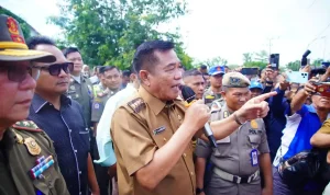 bupati-muba-toha-tohet-audiensi-minyak-rakyat Bupati Musi Banyuasin HM Toha Tohet SH mengenakan seragam dinas cokelat, memegang mikrofon sambil menunjuk ke arah depan saat memberikan arahan tegas di tengah kawalan Satpol PP dan kerumunan warga.