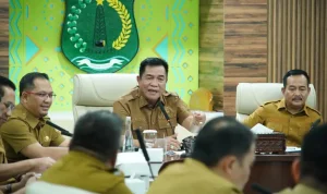 bupati-muba-toha-tohet-rapat-pkm-kemiskinan Bupati Musi Banyuasin H. M. Toha Tohet, S.H. mengenakan baju dinas harian (PDH) cokelat khaki sedang memimpin rapat koordinasi dengan ekspresi serius dan tangan kanan memberikan gestur penekanan di meja.