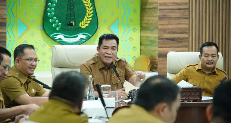 bupati-muba-toha-tohet-rapat-pkm-kemiskinan Bupati Musi Banyuasin H. M. Toha Tohet, S.H. mengenakan baju dinas harian (PDH) cokelat khaki sedang memimpin rapat koordinasi dengan ekspresi serius dan tangan kanan memberikan gestur penekanan di meja.