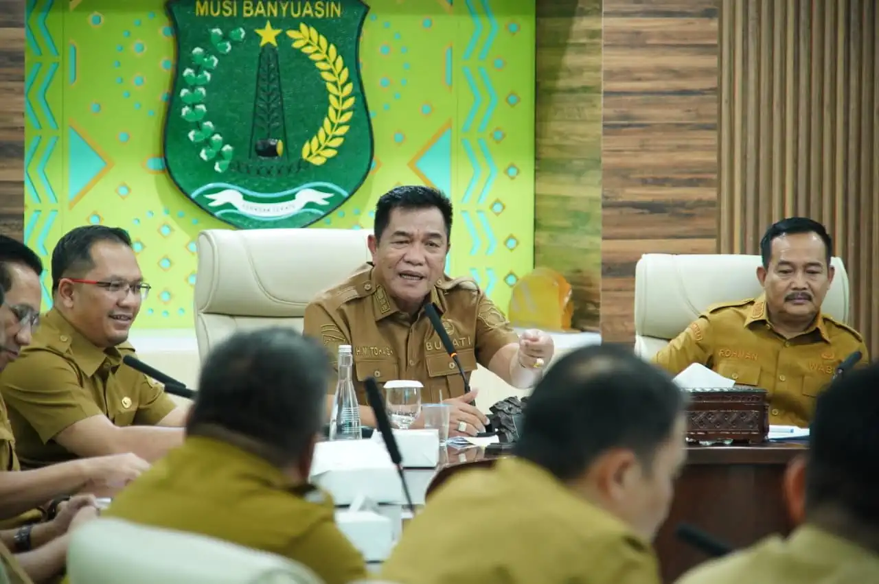 bupati-muba-toha-tohet-rapat-pkm-kemiskinan Bupati Musi Banyuasin H. M. Toha Tohet, S.H. mengenakan baju dinas harian (PDH) cokelat khaki sedang memimpin rapat koordinasi dengan ekspresi serius dan tangan kanan memberikan gestur penekanan di meja.