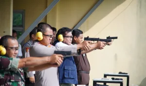 bupati-toha-tohet-lomba-menembak-polres-muba Bupati Musi Banyuasin H. M. Toha Tohet, S.H. mengenakan rompi biru navy di atas kemeja putih, berkacamata pelindung, dan memakai earmuff kuning, sedang membidik sasaran menggunakan pistol dengan kedua tangan lurus ke depan di lapangan tembak terbuka. Di barisannya, tampak Kapolres Muba AKBP Ruri Prastowo dan jajaran Forkopimda lainnya juga sedang dalam posisi menembak dengan fokus yang sama.