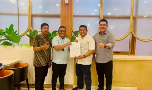 disnakertrans-muba-pertemuan-medco-energi Empat orang pria berdiri berjejer tersenyum di dalam ruangan bernuansa hangat dengan dinding kayu dan jendela besar. Pria kedua dari kiri, Kepala Disnakertrans Muba Herryandi Sinulingga, AP yang berkacamata dan mengenakan kemeja biru muda, tampak menyerahkan map putih berisi surat resmi bersama Manager Medco Energi Hirmawan Eko Prabowo yang mengenakan kemeja putih motif garis vertikal tipis. Di sisi paling kiri dan paling kanan, dua pejabat teknis mengenakan kemeja batik dan kemeja abu-abu kompak memberikan gestur acungan jempol ke arah kamera.