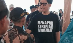handry-pratama-putra-dprd-sumsel-ogan-ilir Anggota DPRD Provinsi Sumsel H. Handry Pratama Putra memakai kaos hitam bertuliskan Menapak Berjejak Berdampak sedang berbincang dengan warga di bawah tenda acara.