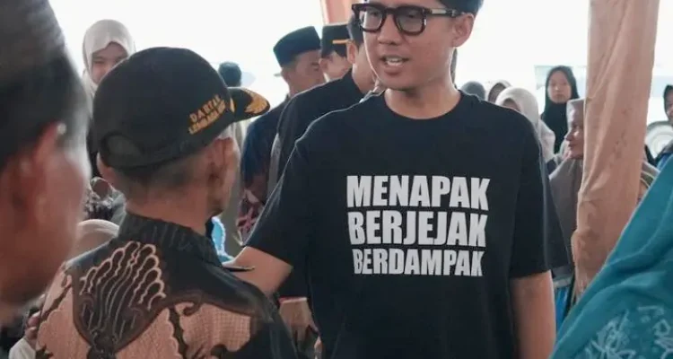 handry-pratama-putra-dprd-sumsel-ogan-ilir Anggota DPRD Provinsi Sumsel H. Handry Pratama Putra memakai kaos hitam bertuliskan Menapak Berjejak Berdampak sedang berbincang dengan warga di bawah tenda acara.