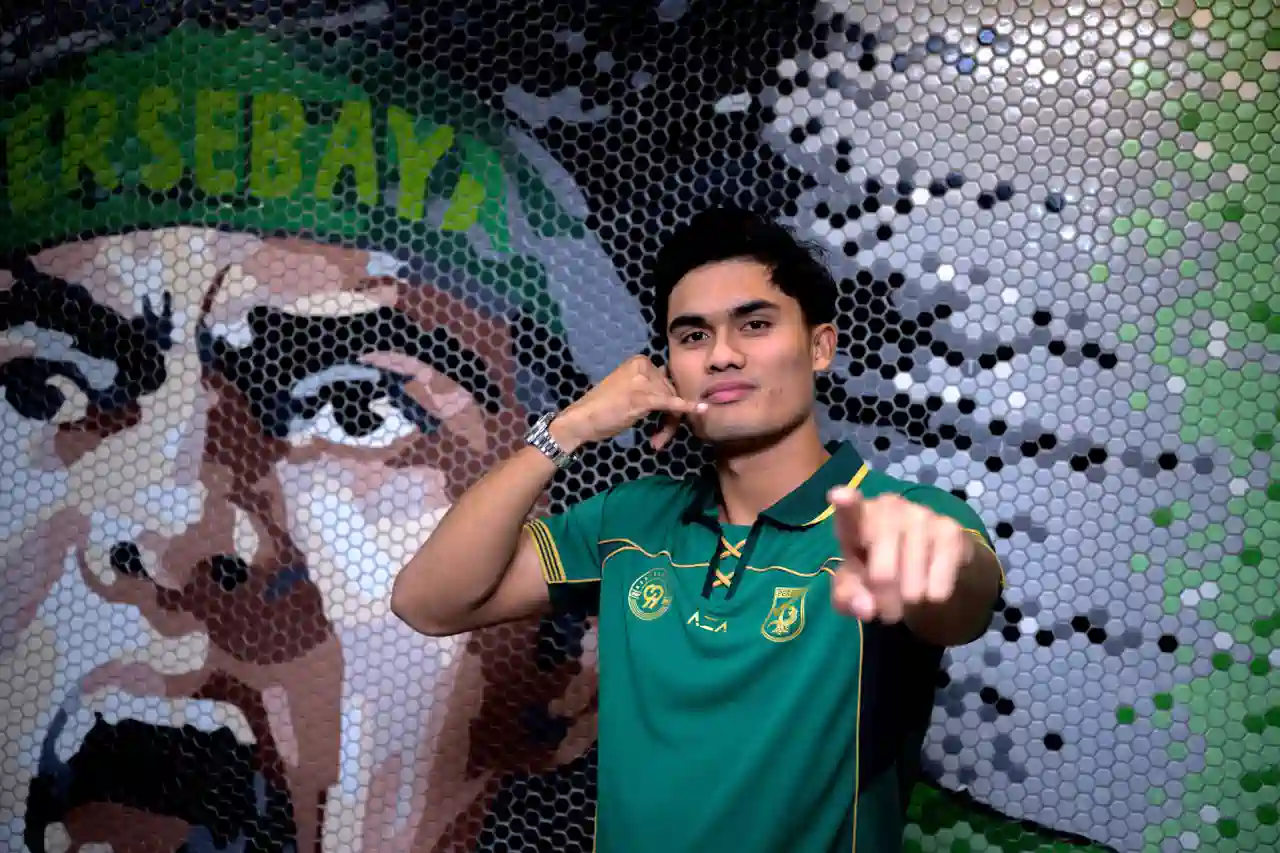 persebaya-surabaya-resmi-rekrut-ramadhan-sananta Penyerang baru Persebaya Surabaya Ramadhan Sananta berpose mengenakan jersey hijau sembari melakukan gestur telepon ikonik di depan mural suporter.