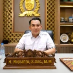 spmb-sma-2026-di-sumatera-selatan-nopianto Wakil Ketua DPRD Provinsi Sumatera Selatan H Nopianto S.Sos M.M duduk di ruang kerjanya dengan latar belakang lambang DPRD Sumsel dan bendera Partai NasDem.