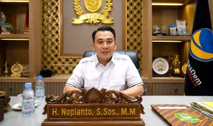 spmb-sma-2026-di-sumatera-selatan-nopianto Wakil Ketua DPRD Provinsi Sumatera Selatan H Nopianto S.Sos M.M duduk di ruang kerjanya dengan latar belakang lambang DPRD Sumsel dan bendera Partai NasDem.
