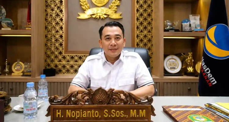 spmb-sma-2026-di-sumatera-selatan-nopianto Wakil Ketua DPRD Provinsi Sumatera Selatan H Nopianto S.Sos M.M duduk di ruang kerjanya dengan latar belakang lambang DPRD Sumsel dan bendera Partai NasDem.