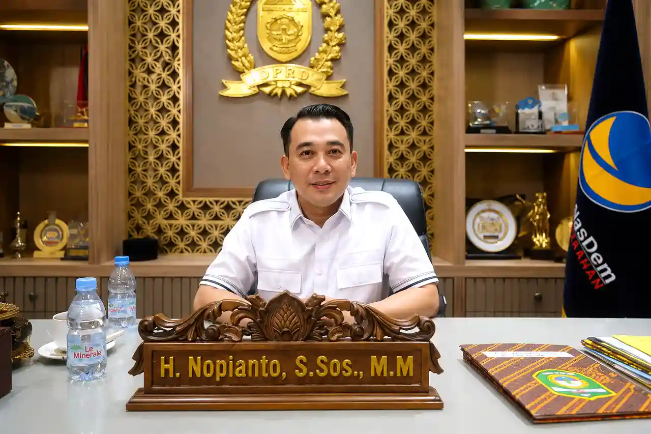 spmb-sma-2026-di-sumatera-selatan-nopianto Wakil Ketua DPRD Provinsi Sumatera Selatan H Nopianto S.Sos M.M duduk di ruang kerjanya dengan latar belakang lambang DPRD Sumsel dan bendera Partai NasDem.