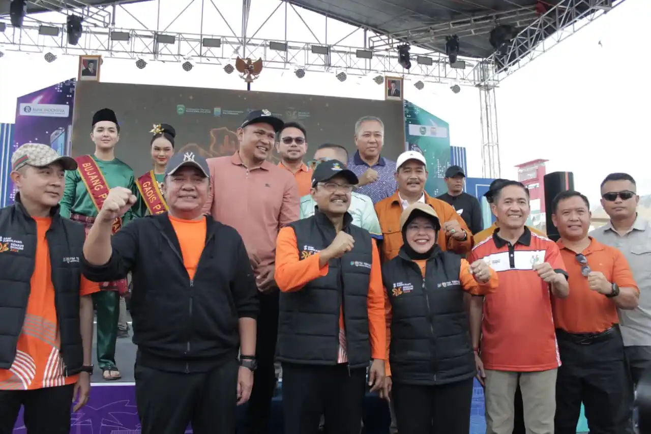 Jajaran pejabat negara dan daerah berdiri bersama di atas panggung luar ruangan dengan latar belakang layar digital besar.